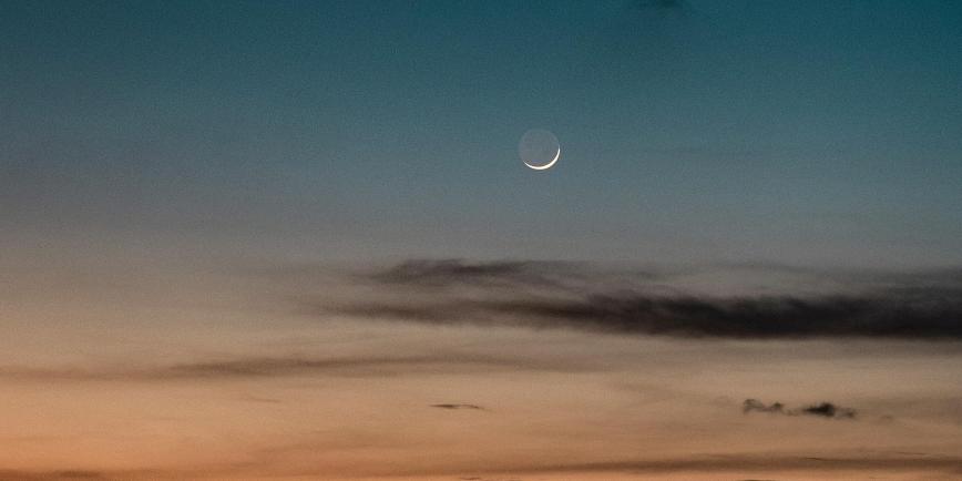 Image of new crescent Moon against the sky with sunset and black clouds