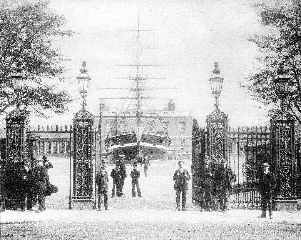 Historic photograph showing the entrance to the Greenwich Hospital School, now known as the Queen's House. Sea cadets in uniform can be seen flanking the iron gates, and a training ship is positioned in the middle of the lawn